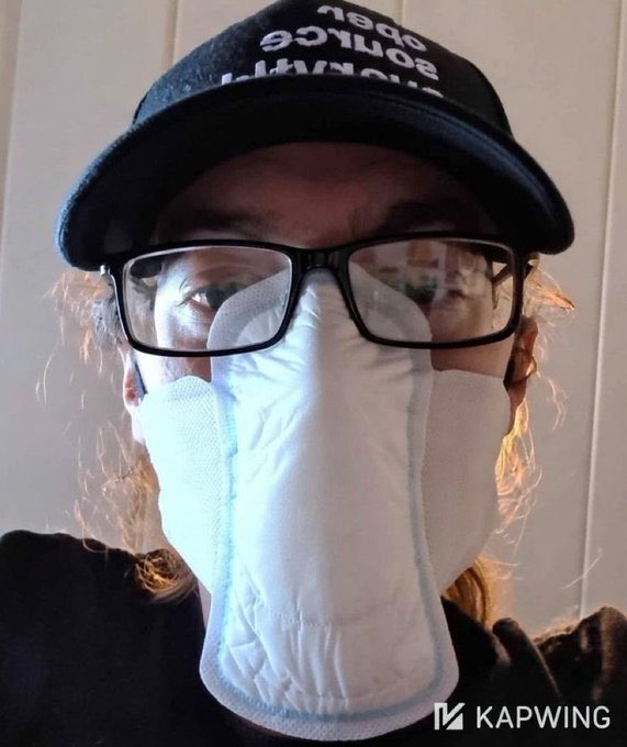 A selfie of a person wearing a black cap with reversed white text reading 'dance yourself clean', black-rimmed glasses, and a large white disposable face mask covering their lower face.