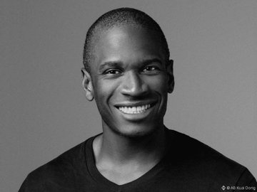 A black-and-white portrait of a smiling young Black man, credited to photographer Rui Dong.