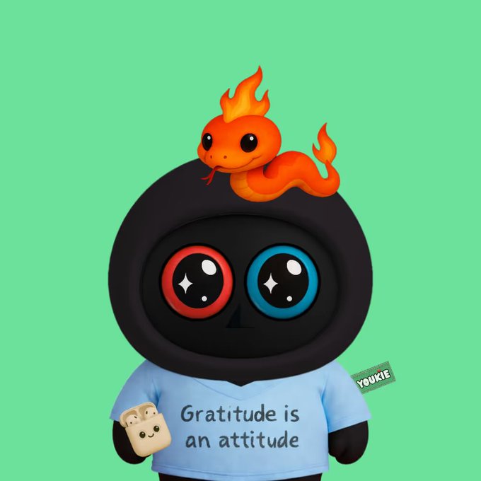 A digital illustration of a black character with mismatched red and blue eyes, wearing a light blue shirt reading 'Gratitude is an attitude,' topped with an orange flame-like snake on its head, with a 'YOUKIE' tag.