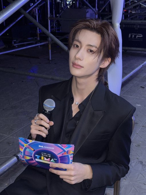 A young man in a black suit holds a microphone and a card reading 'TMEA 2025', seated at what appears to be an event stage.
