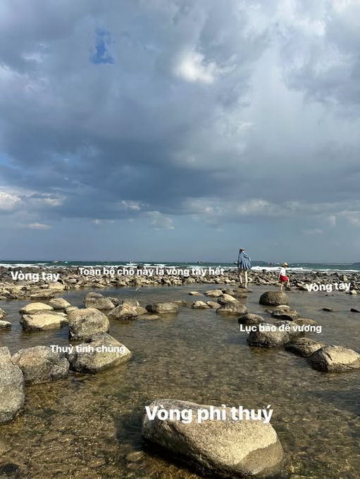 A coastal scene with rocks in shallow water under a cloudy sky, featuring a person and child walking in the distance, overlaid with Vietnamese text including 'Vòng tay', 'Toàn bộ chỗ này là vòng tay hết', 'Thụy tinh chúng', 'Lục bảo đá vương', and 'Vòng phi thuỷ'.