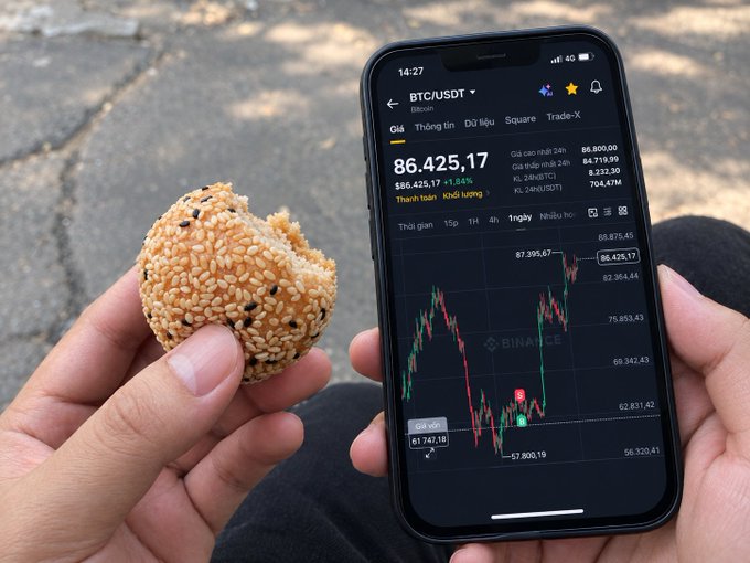 A person holds a half-eaten sesame-coated pastry in one hand while checking the Bitcoin (BTC/USDT) price chart on the Binance app with the other, where BTC is displayed at $86,425.17 with a +1.84% gain—capturing the essence of a trader's Monday morning routine of checking the markets over a quick breakfast while hoping for bullish momentum.