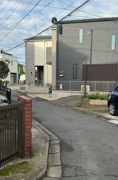 A residential street with modern two-tone gray townhouses, where a bicycle is parked along the narrow alley. The original poster expected to spot a Shiba Inu but was mistaken, likely misidentifying another object or feature in the scene.
