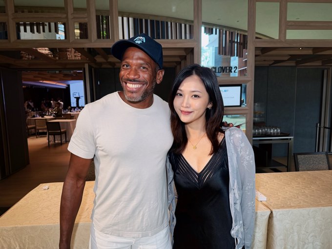 The image shows a smiling man wearing a navy cap and white t-shirt posing alongside an elegant woman in a black dress with sheer sleeves at what appears to be an upscale restaurant or event venue with "CLOVER 2" visible in the background. The caption suggests the man is CryptoHayes, likely Arthur Hayes of BitMEX, whom the poster met at a business/networking event.