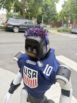 A robot wearing a USA #10 jersey and patriotic star-spangled headpiece stands on a sidewalk in South Park, matching the post's mention of a Photon robot being spotted in the area.