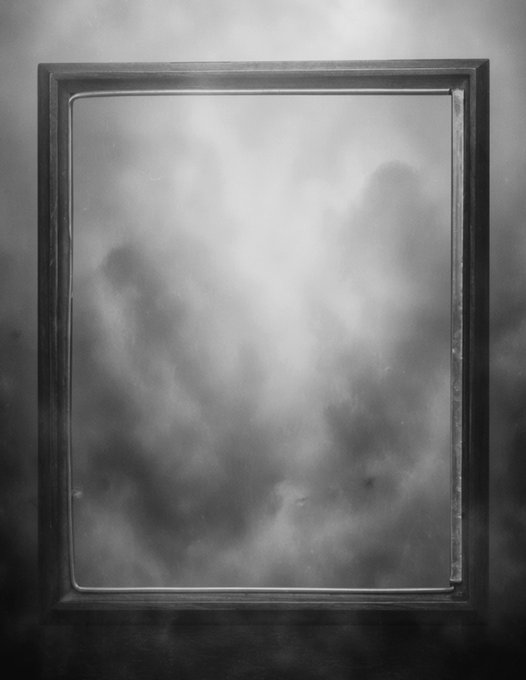 A black and white artistic photograph of an empty picture frame with misty, fog-like reflections obscuring its glass surface.