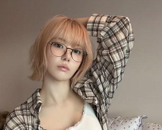A young woman with light brown hair and round glasses wears a plaid overshirt, posing casually with her arm behind her head. The image accompanies a "GM X" post expressing support for a user while highlighting the positive sentiment behind the early morning greeting.