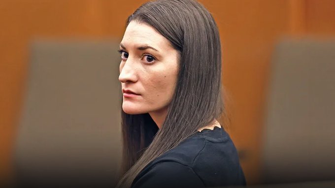 A young woman with long dark hair, wearing a black shirt, looks over her shoulder in what appears to be a courtroom setting.