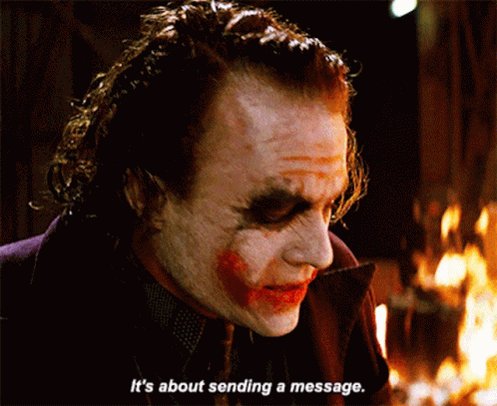 The image features a man with spiky hair, wearing a purple jacket, who appears to be a character from the movie The Dark Knight. He has red makeup on his face, giving him a distinctive look. In front of him, there is text that reads "It's about sending a message." This suggests that the person in the image might be promoting or discussing the movie The Dark Knight and its themes, such as the importance of communication and understanding.