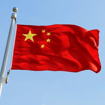 The Chinese national flag waves against a blue sky. The image accompanies a report that Chinese authorities are seeking to confiscate 61,800 Bitcoin—valued at about $5.7 billion—linked to a fraud that harmed over 102,000 investors.