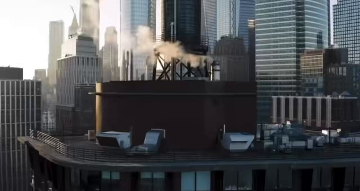 The image shows an aerial view of a city skyline with tall buildings, including skyscrapers that are illuminated by sunlight. The sky above the city appears hazy, creating a unique atmosphere. In the foreground, there's a large building with a chimney emitting smoke from it. Below this building is another structure, and in the background, more buildings can be seen. A caption below the image reads "GM everyone GM GM $BOMI homies Have a fabulous day".