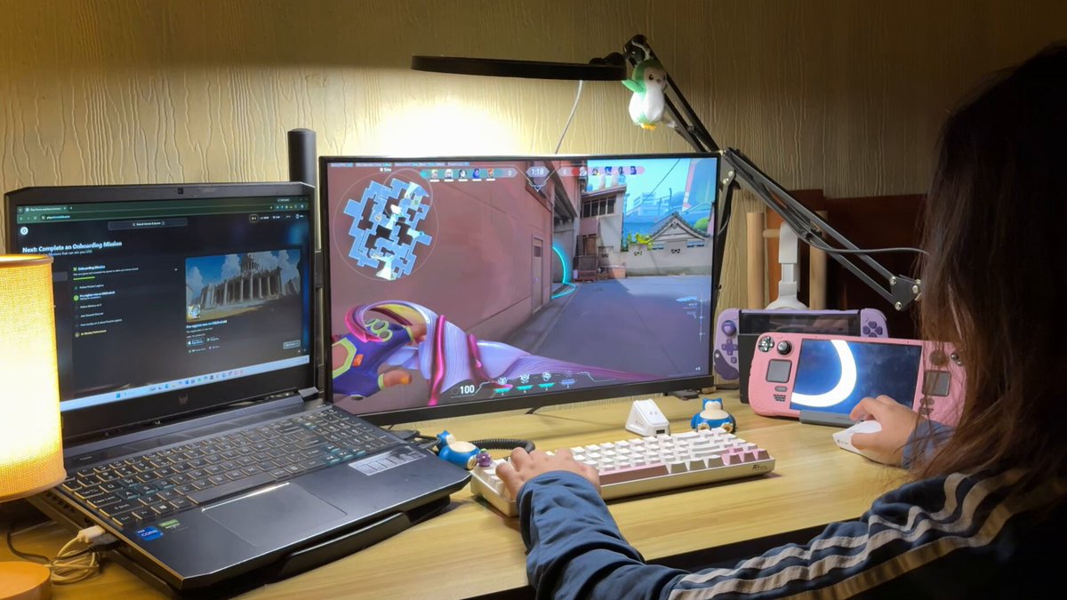 The image shows a person sitting at a desk with a laptop computer open in front of them. The laptop screen displays an image of a character from a video game called @Immutable, which has been described as "cozy" by one user. A keyboard and mouse are also present on the desk next to the laptop.