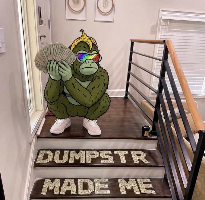 A green gorilla character cutout wearing sunglasses and a banana hat, sitting on stairs holding a fan made of dollar bills, with money arranged on the steps spelling 'DUMPSTR MADE ME'.