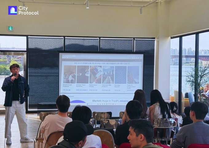A presenter stands before an audience at a co-hosted event showcasing City Protocol's vault infrastructure and Onchain Token Portfolios in Korea, with the projection screen displaying project information alongside partners SmartXTerminal, StableStock, KaitoAI, De1.ai, yzilabs, and BNB Chain.