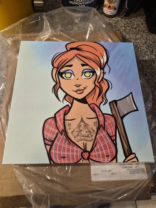 A canvas painting of a cartoon-style red-haired woman with yellow eyes wearing a red plaid shirt and holding an axe, sitting on a countertop in plastic packaging.