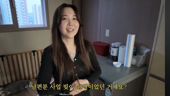 A young Korean woman with long dark hair speaking indoors, with Korean subtitles reading '남편분 사업 빛이 40억이었던 거예요?' at the bottom.