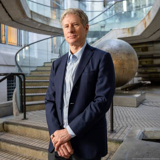 A man with gray hair wearing a navy blue blazer and light blue shirt stands confidently in front of a spiral staircase, with a credit watermark reading 'San Francisco Business Times 2024' in the bottom right corner.