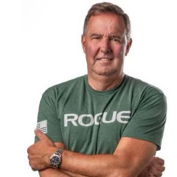 A middle-aged man with short gray hair stands confidently with his arms crossed, wearing a green "ROGUE" t-shirt and a watch, matching Lawrence Lepard's appearance as he warns about fiat currency's inevitable failure and the urgent need to transition to Bitcoin.