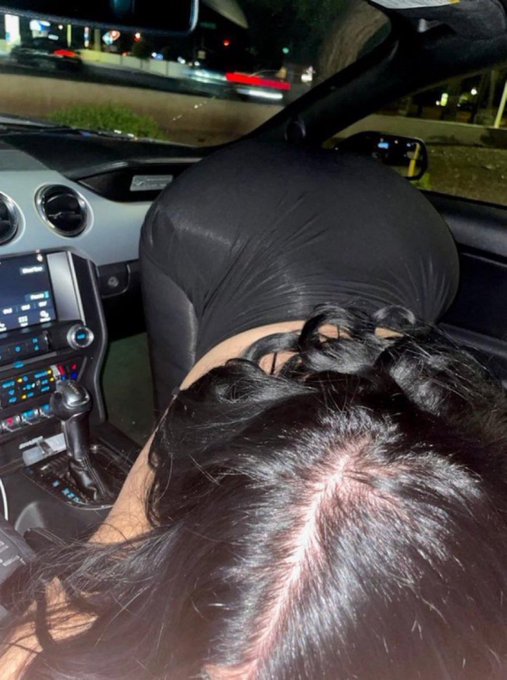 A woman lies across the front passenger seat of a Mustang at night with her dark hair fanned out, seemingly knocked out cold by a jaw-dropping crypto revelation. The post jokes that the shareable photo of her passed out was her reaction to learning how much $Basecat (Basecat) the poster owned.