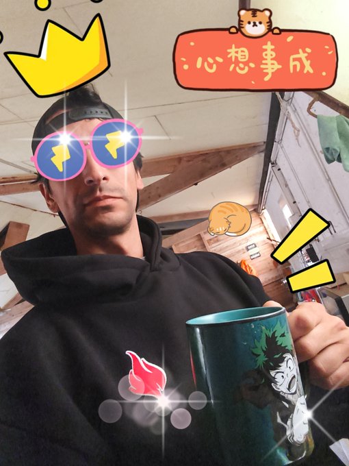 A selfie of a young man wearing a black hoodie and a backwards cap, decorated with digital stickers including a crown, pink sunglasses, and a red banner with Chinese text '心想事成' (May all your wishes come true).