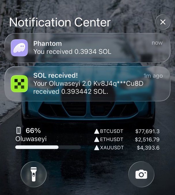 A Phantom wallet notification center screenshot showing received SOL tokens (0.3934 SOL) with cryptocurrency prices for BTCUSDT ($77,691.3), ETHUSDT ($2,516.79), and XAUUSDT ($4,393.6) over a background of a car.