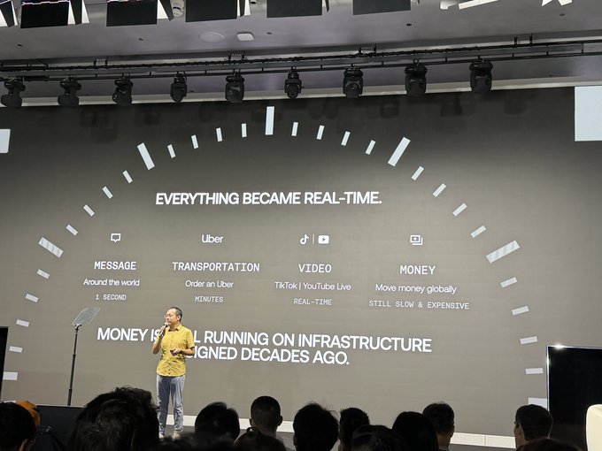 A presenter stands on stage in front of a large screen titled 'EVERYTHING BECAME REAL-TIME,' illustrating how message, transportation (Uber), video (TikTok/YouTube Live), and money services have evolved.