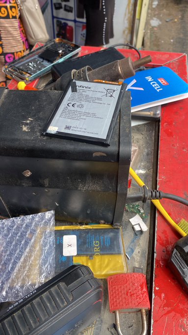 Photograph of a workbench with an Atrix soldering iron charger, a multimeter, IntelliCELL packaging, bubble wrap, and various electronics tools and components scattered on a red surface.
