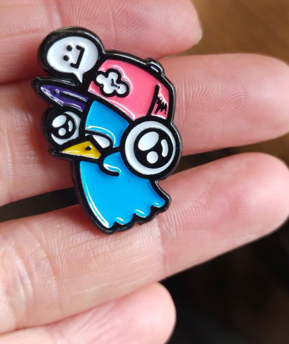 A close-up of a colorful enamel pin featuring cartoon characters and ghost-like faces held between fingers.