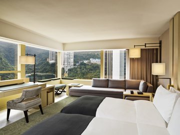 A luxurious hotel suite featuring floor-to-ceiling windows with stunning city and mountain views, elegant modern furnishings including a plush bed, gray sofa, and contemporary lighting. The image showcases the sophisticated interior of The Upper House in Hong Kong, reflecting the post's description of the ultra-luxury 5-star hotel's Studio 80 Island View room.