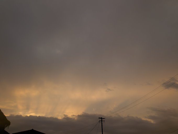 A dramatic cloudy sky at dusk with crepuscular rays (sunbeams) breaking through the clouds, with power lines and a utility pole visible in the lower right.