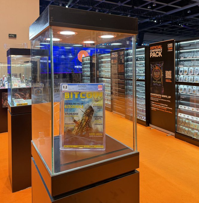 A graded CGC 9.8 "BITCOIN: The Rise and Fall of Bitcornics" comic book from Bitcoin Magazine's 2012 issue is displayed in a glass case at the Bitcoin Conference Asia merch store. The exhibit sits next to an "OFFICIAL CONFERENCE PACK" display and shelving filled with Bitcoin-themed magazines, confirming the post's mention of the rare comic and complete "Genesis Box" magazine set available at the venue.