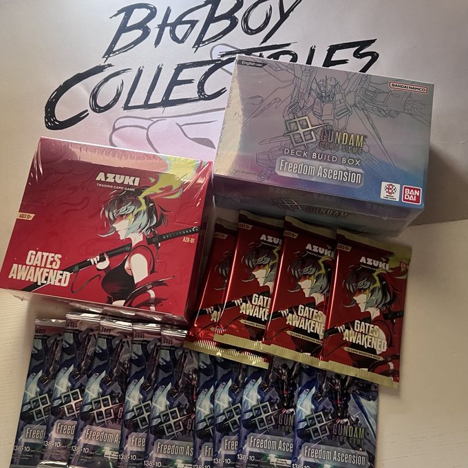 A Gundam Card Game collection featuring an Azuki Trading Card Game "Gates Awakened" booster box and several packs alongside a "Gundam Card Game Deck Build Box: Freedom Ascension" from Bandai Namco, likely part of a stream haul.