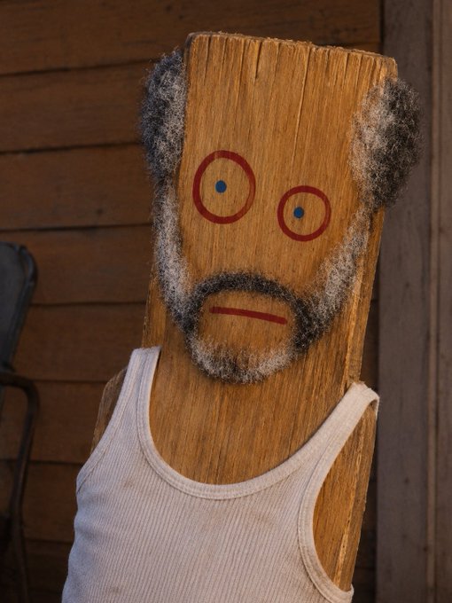 This image shows a wooden plank person with a white tank top, eyes and beard drawn on it, humorously relating to the post's warning against pumping $plank over 400k.