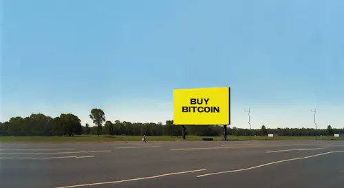 A photograph of a bright yellow billboard in an empty parking lot displaying 'BUY BITCOIN' in black text.