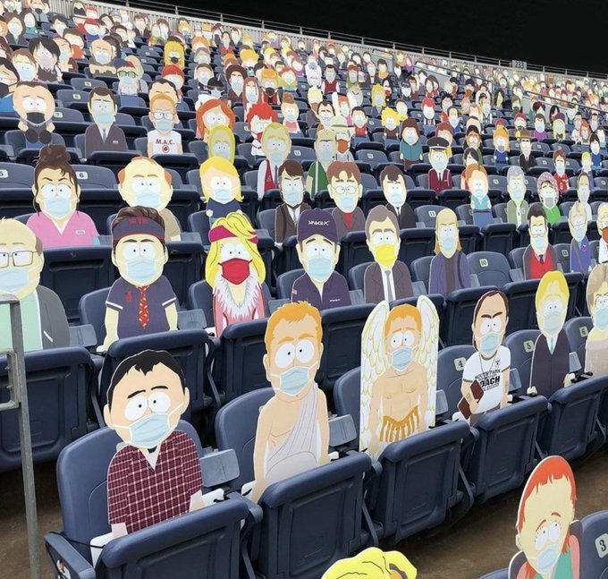 The image shows a large crowd of people wearing face masks gathered together in an indoor space, possibly at a stadium or event venue. The audience appears to be engaged with the content being displayed on the walls around them, which includes various cartoon characters and logos. Some of these characters are wearing masks as well, adding to the overall theme of the scene. The atmosphere seems lively and interactive, with people actively participating in the experience by wearing face masks while watching the content or taking photos.