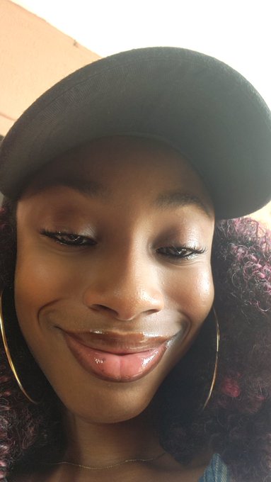 The image features a woman wearing a black baseball cap, smiling at the camera while looking directly into it. She has curly hair that adds a unique touch to her appearance. The caption of the image includes the words "Gn CT Calling it a day here... Stay with @NomismaNetwork and @wallchain See y'all tomorrow". This suggests that the woman might be sharing some personal information or experiences related to the post, possibly about her day or her connection to the network.