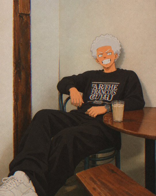 A person sits relaxed at a wooden café table with a glass beverage, wearing a black sweater that reads 'FARTHE FRANÇOIS CUBU PARIS' and an animated face mask featuring white hair and a grimacing expression.