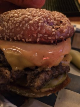 A close-up photo of a large, messy hamburger with a sesame seed bun, melted cheese, and meat patties being held by a hand.