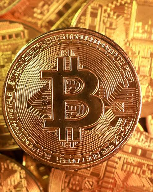 A close-up image of a gold-colored Bitcoin coin resting on other coins.
