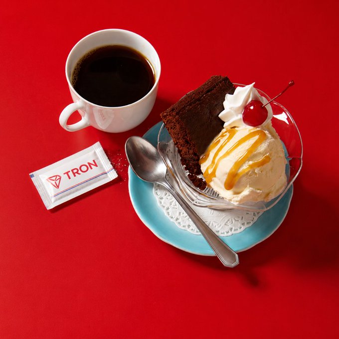 A cup of black coffee sits beside a decadent chocolate cake sundae topped with vanilla ice cream, caramel drizzle, whipped cream, and a cherry on a turquoise plate, while a sugar packet labeled "TRON" rests nearby—visually punning on the post's "Good morning" greeting with the TRON ticker.