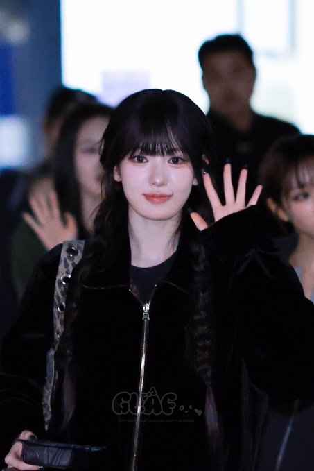 A photograph of a young woman with long dark hair waving, dressed in a black velvet zip-up top, with a 'GF' watermark on the image.