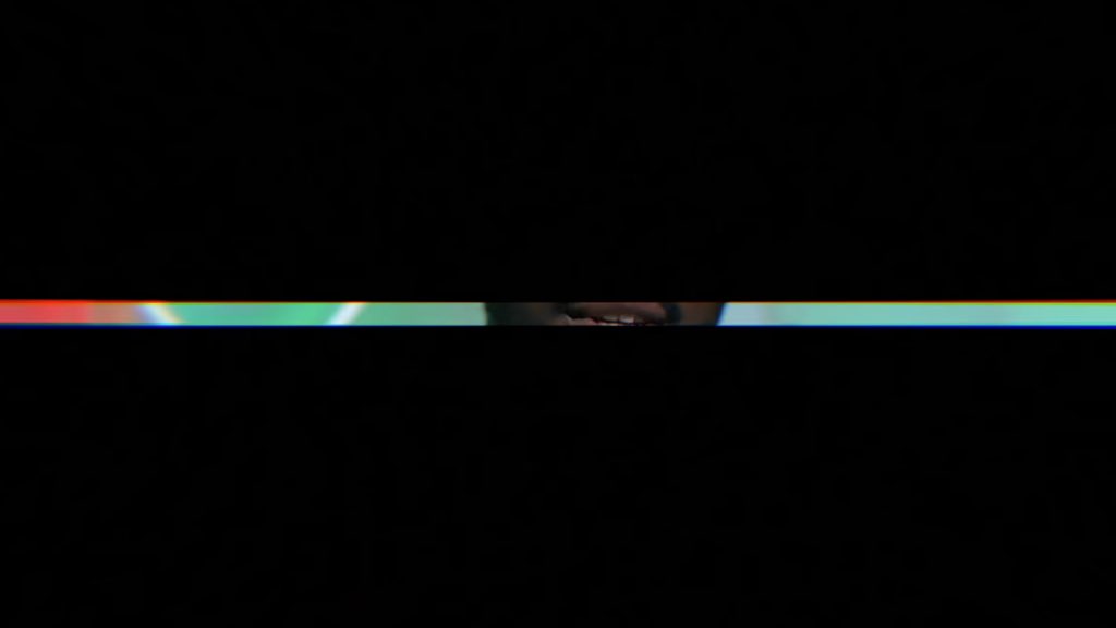 A mostly black image with a thin, glitch-like horizontal strip of color across the middle, showing red, green, and blue hues with a faint blurry object visible.