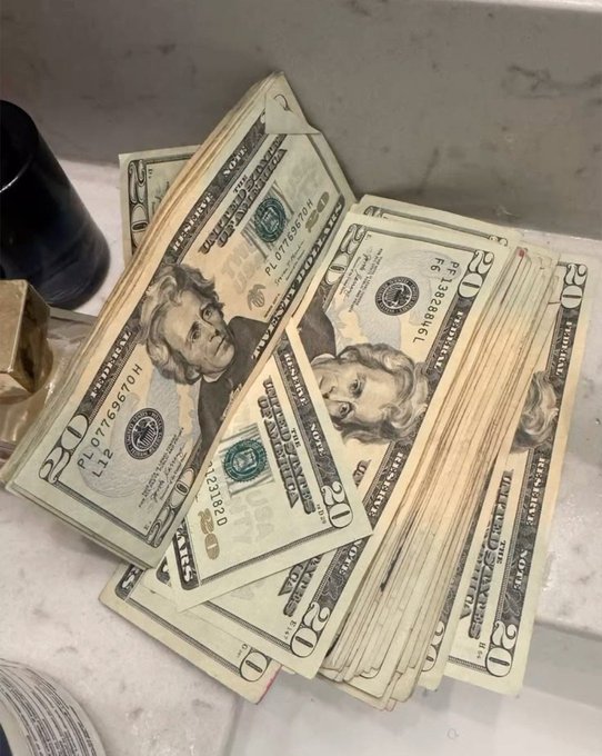 A stack of U.S. twenty-dollar bills, featuring Andrew Jackson's portrait and serial numbers such as "PL07766701H" and "L63186861L," is spread across a marble countertop, visually reinforcing the post's message about pursuing wealth and resisting poverty.