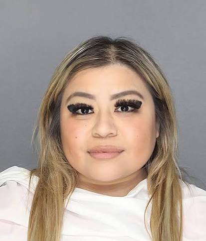 A selfie of a young woman with long blonde-highlighted hair, heavy eyelashes, and a nose piercing, posing against a gray background.