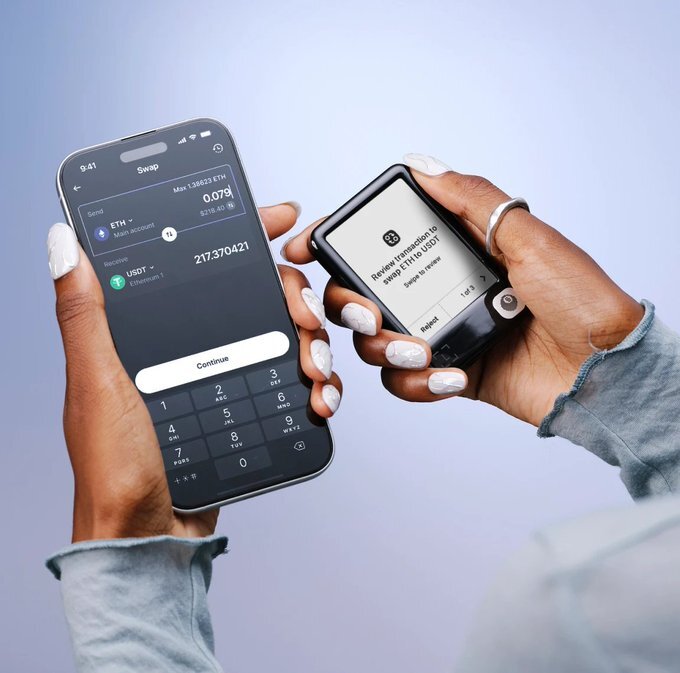 A close-up of a person's hands with white manicured nails holding a smartphone displaying a crypto swap interface (sending 0.079 ETH for 217.37 USDT) alongside a hardware wallet prompting to review the transaction.
