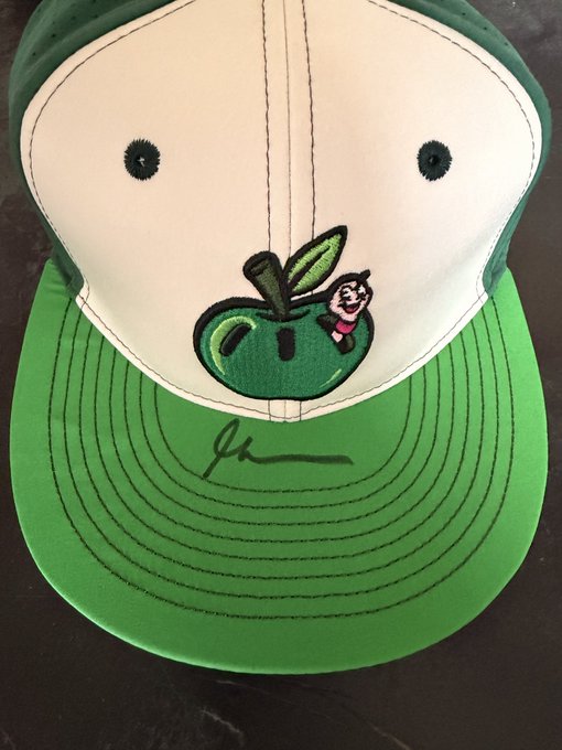 A green and white snapback hat featuring an embroidered apple design with a cartoon character (resembling the Honeycrisp mascot) and a signature on the brim.