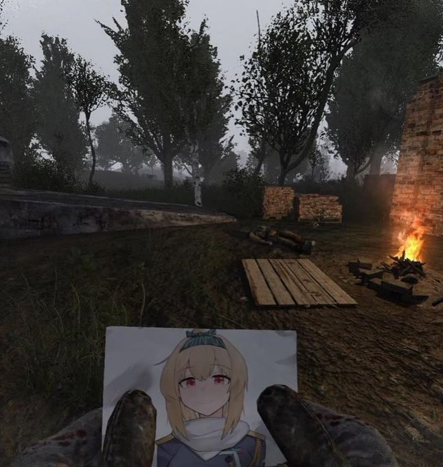 A first-person view from a video game, showing the player holding an anime-style printout, with a foggy outdoor environment, trees, a campfire, and wooden pallets in the background.
