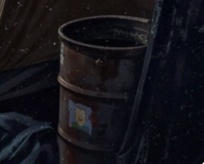 A close-up shot of a rusty metal barrel with a small label showing a teddy bear, set in a dark, shadowy environment.
