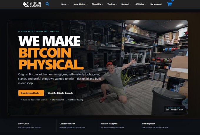 A website homepage screenshot for 'Crypto Cloaks' featuring the headline 'WE MAKE BITCOIN PHYSICAL' alongside an image of a man kneeling in a shop/workshop surrounded by products, with navigation links like 'Shop', 'Home Mining', and 'About Us'.