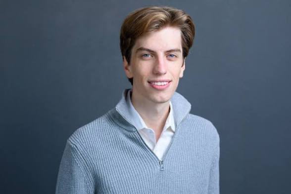 A young man with light brown hair smiles subtly while wearing a gray zip-up sweater over a white collared shirt, posed against a dark gray background. The image of a confident, smiling individual contrasts with the post's cynical warning about market cycles and being "exit liquidity," suggesting that the naive optimism seen in the subject is exactly what gets exploited during speculative bubbles.